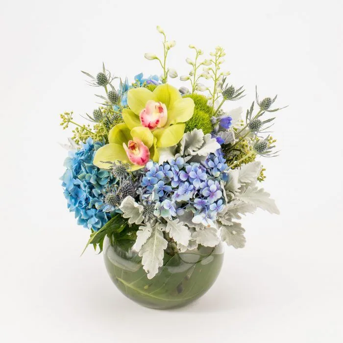 Cool blue hydrangea, green cymbidium orchid, sea-holly and dusty-miller in a low green glass fishbowl — Blue Eclipse